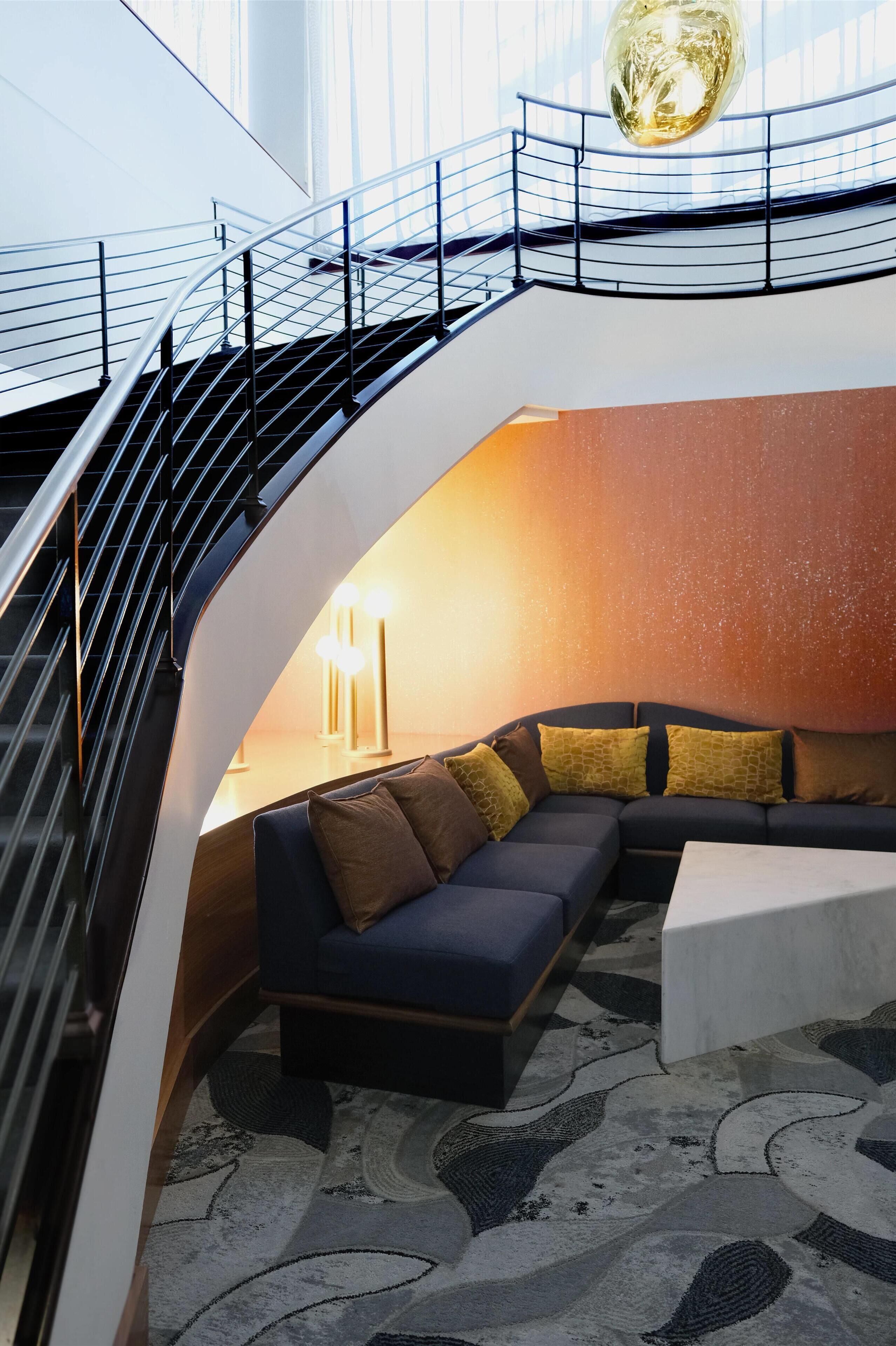 A curved staircase with metal railings, a sectional sofa with multiple cushions, a white coffee table, and a patterned rug.