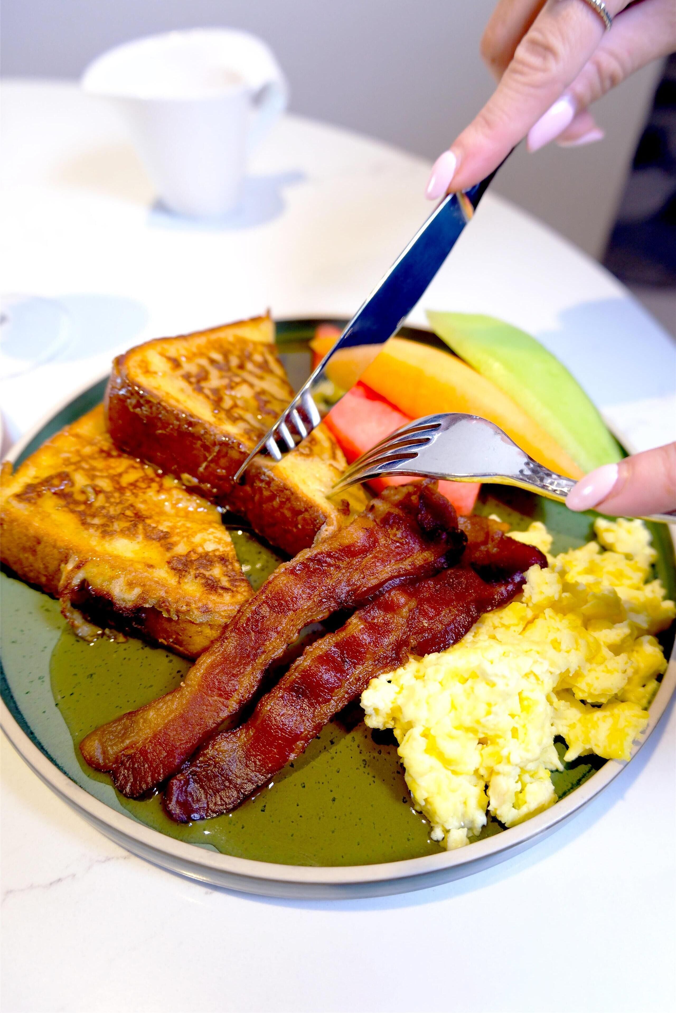 A breakfast plate with toast, bacon, scrambled eggs, and a slice of melon.