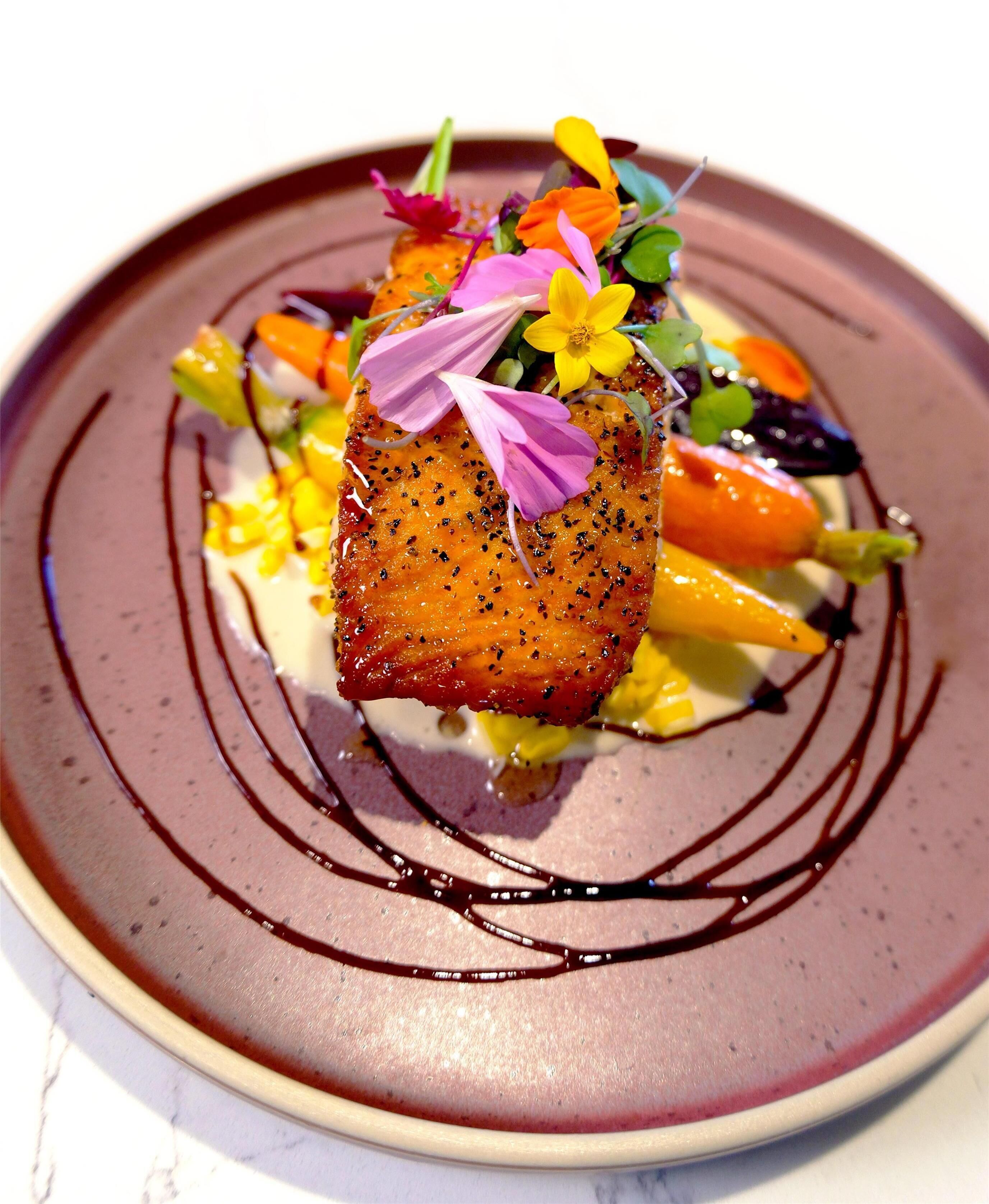 A plate with a piece of salmon, vegetables, and a decorative flower arrangement.