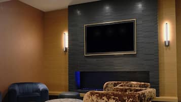 Uma sala de estar moderna com uma televisão de tela plana fixada numa parede texturizada, um sofá de couro escuro, um banquinho estampado e uma mesa de centro de mármore.