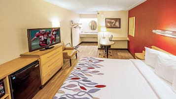 A hotel room with a bed, a desk with a television, a bathroom, and a dining area.