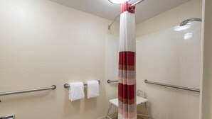 Un baño con cortina de ducha, barras de apoyo y un perchero para toallas.