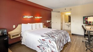 Habitación de hotel con cama, mesita de noche, lámpara, escritorio, silla y un baño visible a través de una puerta abierta.
