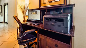 Una oficina de hotel con una computadora de escritorio, una impresora y una silla.