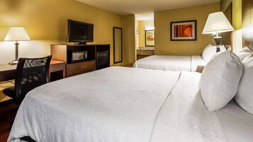 A hotel room with two beds, a desk with a computer and a TV, a microwave, and a small refrigerator.