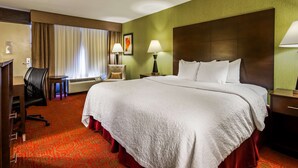 Una habitación de hotel con una cama grande, un escritorio, una silla, una mesa y una ventana con cortinas.