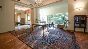 Un salón amplio con un gran tapiz estampado, una araña y vistas al exterior.