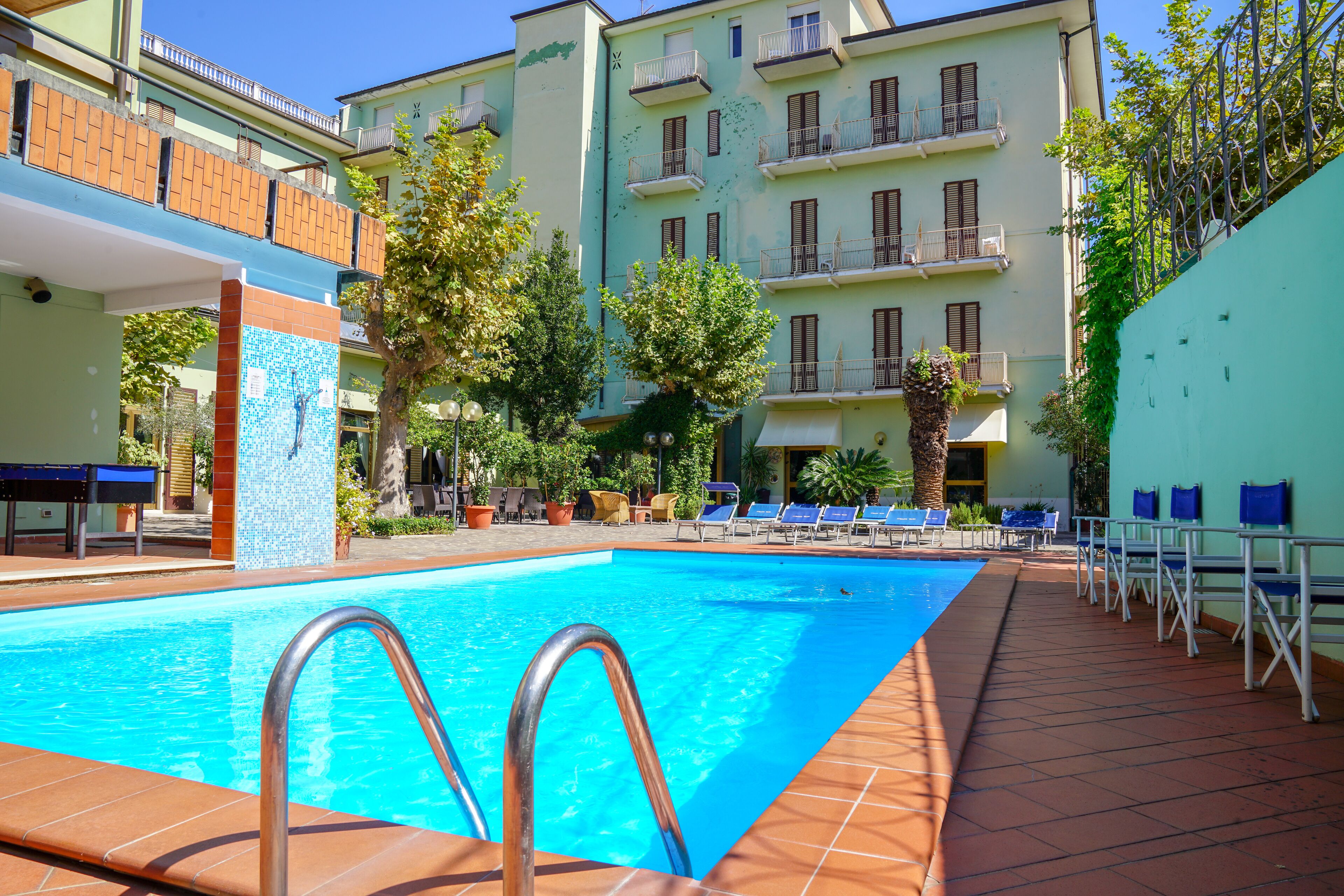 Una piscina con escalera metálica, rodeada de sillas de descanso y plantas en macetas.