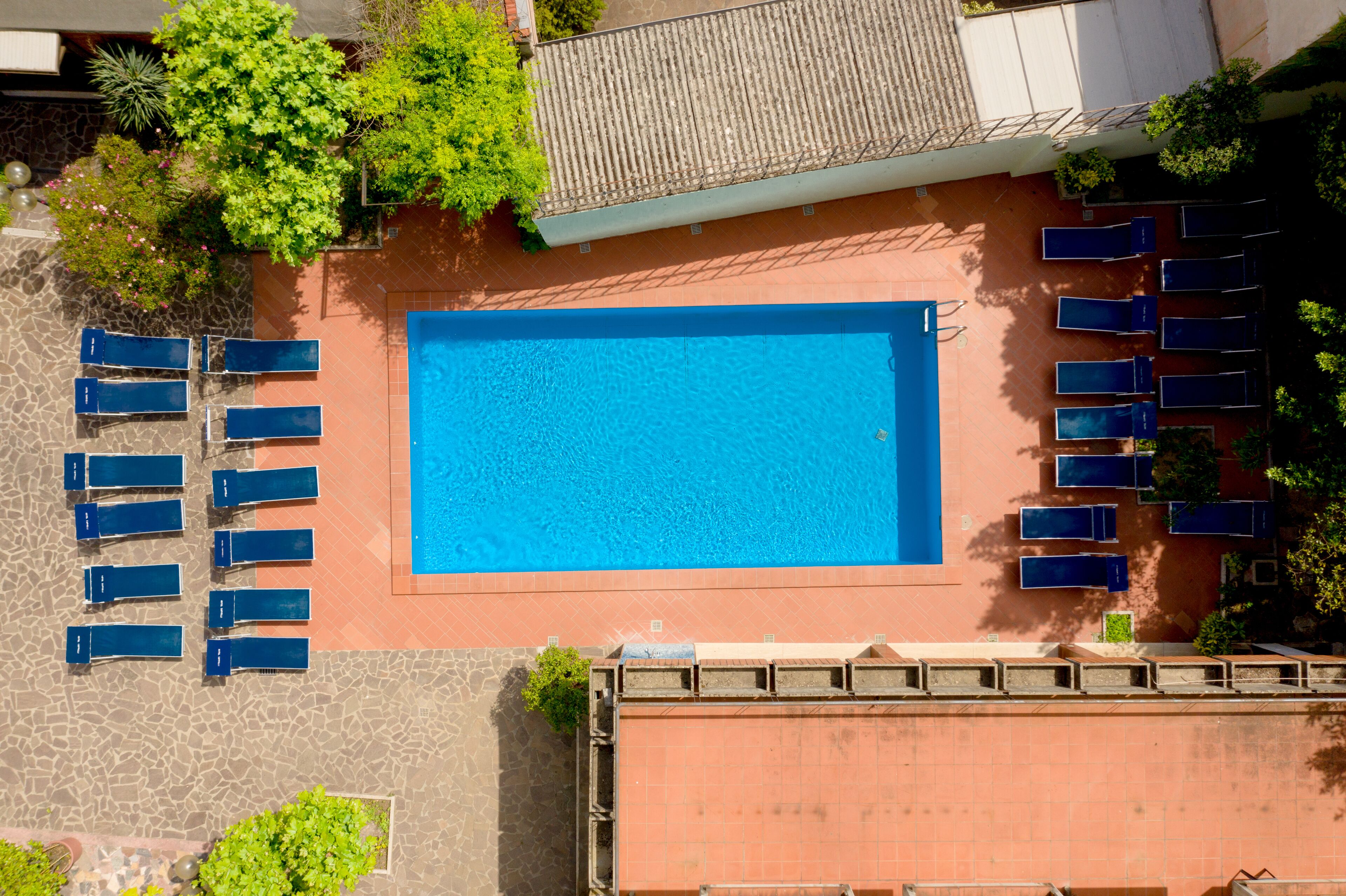 An aerial view of a swimming pool with adjacent lounge chairs and a tiled patio area.