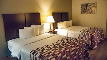 A hotel room with two beds, a nightstand, a lamp, and a wall-mounted artwork.