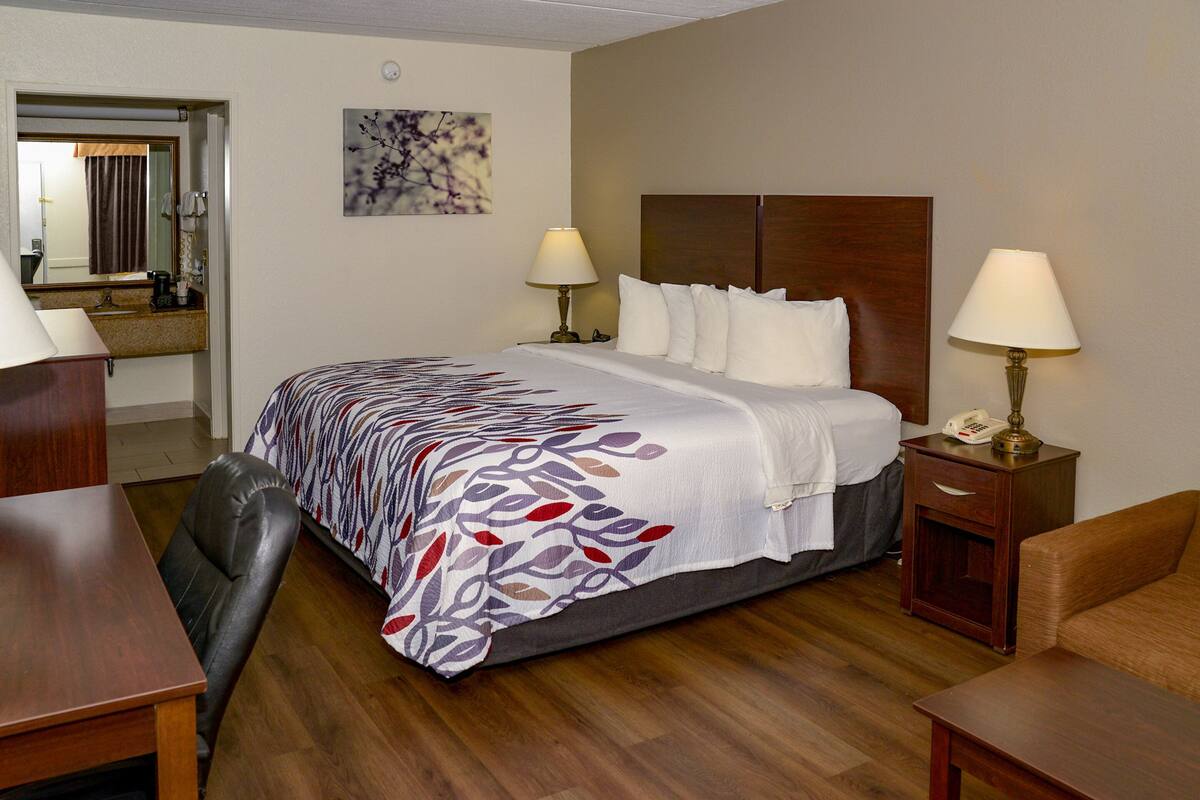 A hotel room with a large bed, two bedside tables with lamps, a wooden desk, a chair, and a small table.