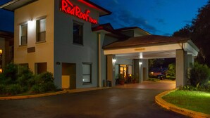 Un edificio de dos plantas con un letrero de 'Red Roof Inn', un acceso cubierto y un área de estacionamiento.