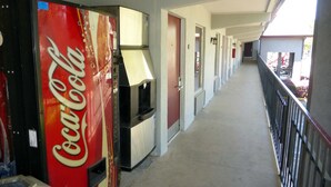 Un pasillo con una máquina expendedora de Coca-Cola, puertas y un balcón con barandilla.