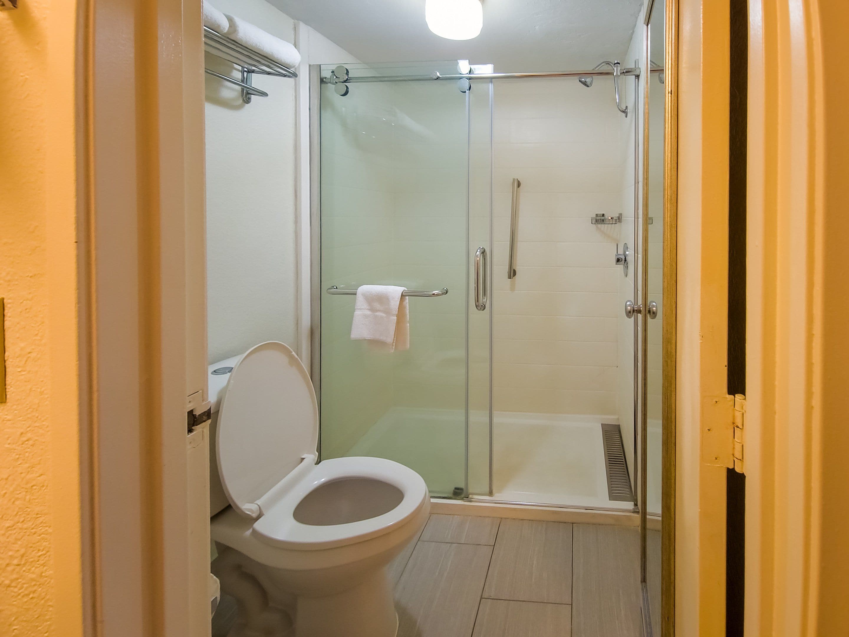 Un baño con inodoro, cabina de ducha de vidrio y toallero.