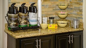 Una encimera de cocina con cafeteras, una pila de tazas y un escurreplatos.