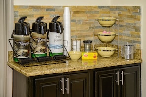 A kitchen counter with coffee makers, a stack of cups, and a dish rack.