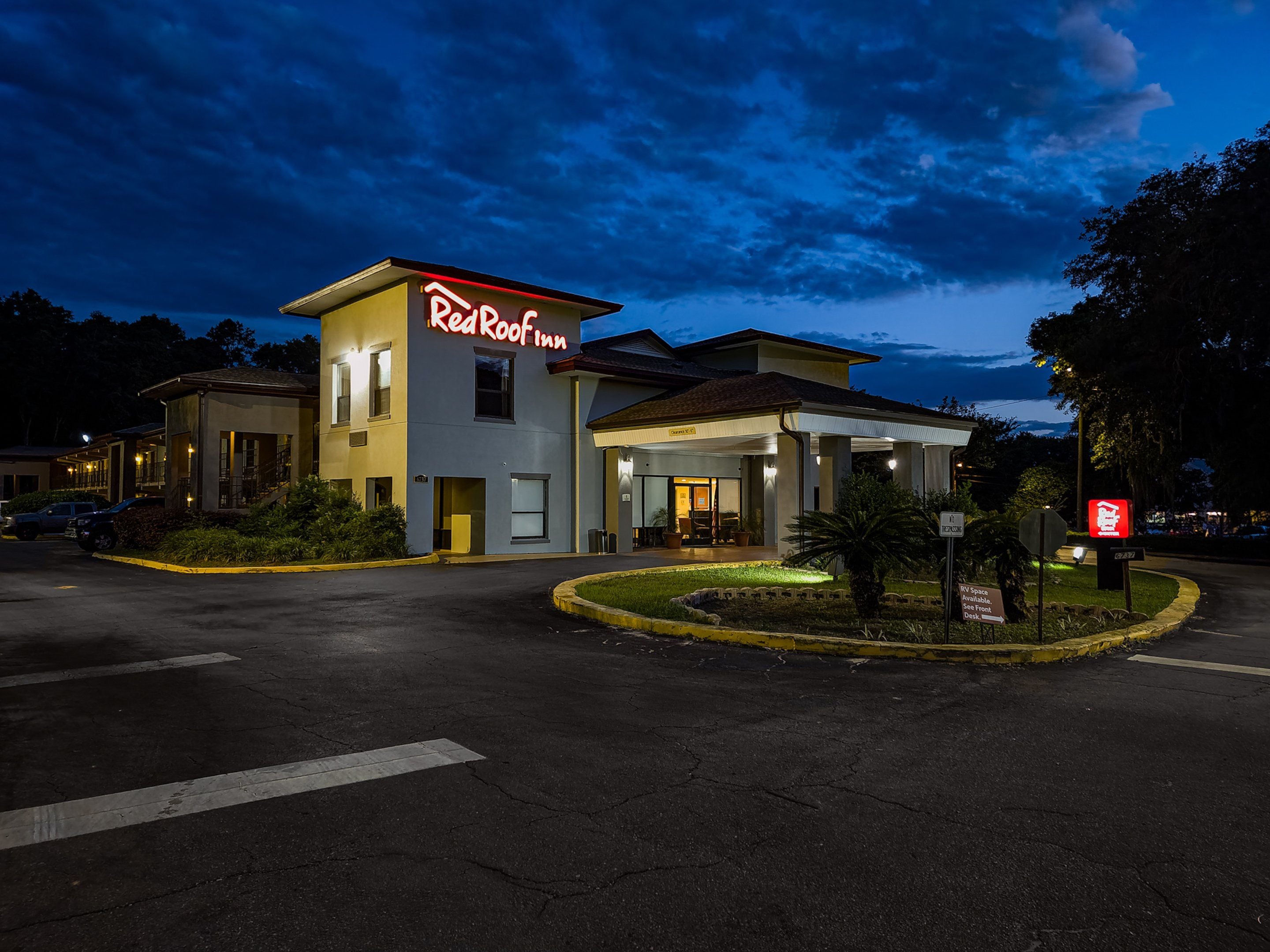 Un hotel Red Roof Inn con una entrada bien iluminada, un estacionamiento y un letrero que indica disponibilidad para vehículos recreativos.