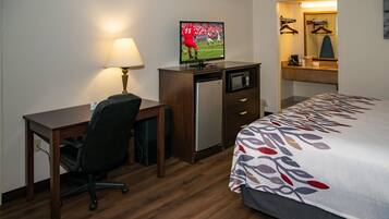 A hotel room with a bed, a desk, a chair, a television, a refrigerator, a microwave, and a mirror.