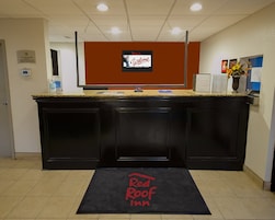 Una recepción con una pantalla digital mostrando un mensaje de bienvenida, el letrero de Red Roof Inn y un felpudo en la entrada.