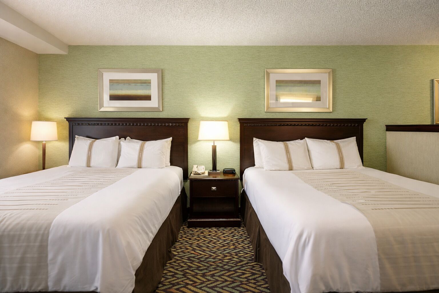 A hotel room with two beds, a nightstand with a lamp, and a patterned carpet.