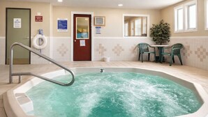 A hot tub with a metal ladder, a door with a sign, a small table with chairs, and a potted plant. - Fireside Inn and Suites (Devils Lake)