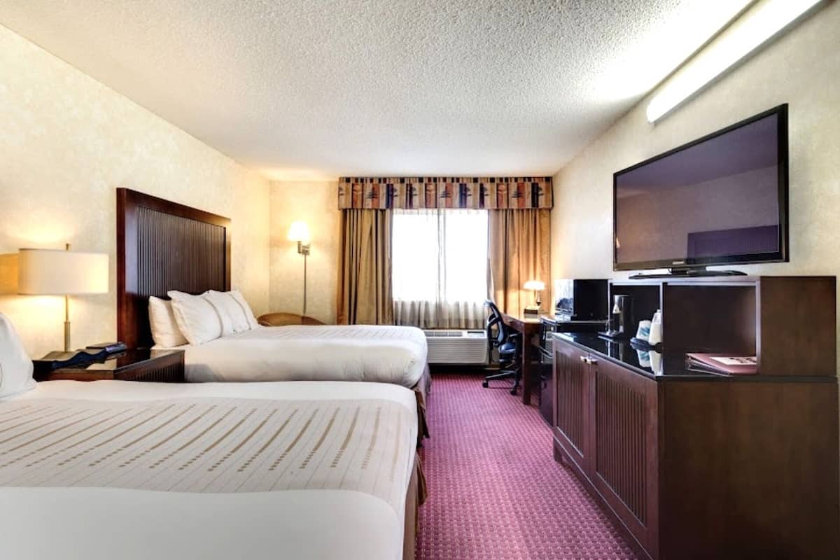 A hotel room with two beds, a desk, a television, and an air conditioning unit.