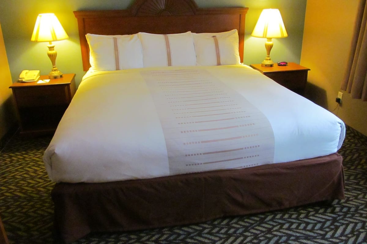 A hotel room with a large bed, two bedside lamps, a telephone, and a nightstand.