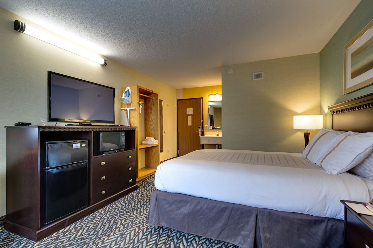 A hotel room with a bed, a TV, a desk with a computer, a mirror, and a lamp.
