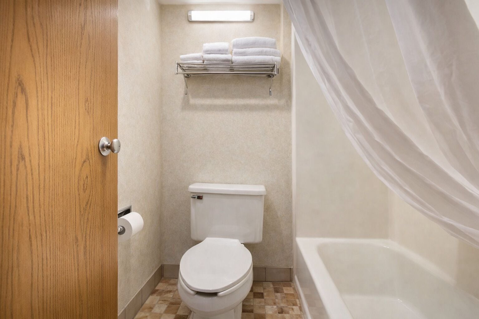A bathroom with a toilet, a shelf with folded towels, and a bathtub.