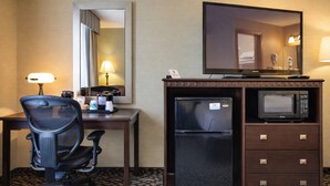 A hotel room with a desk, chair, mirror, television, refrigerator, microwave, and a minibar. - Fireside Inn and Suites (Devils Lake)