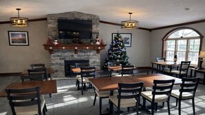 A dining area with tables and chairs, a fireplace, a Christmas tree, and a large window. - Fireside Inn and Suites (Devils Lake)