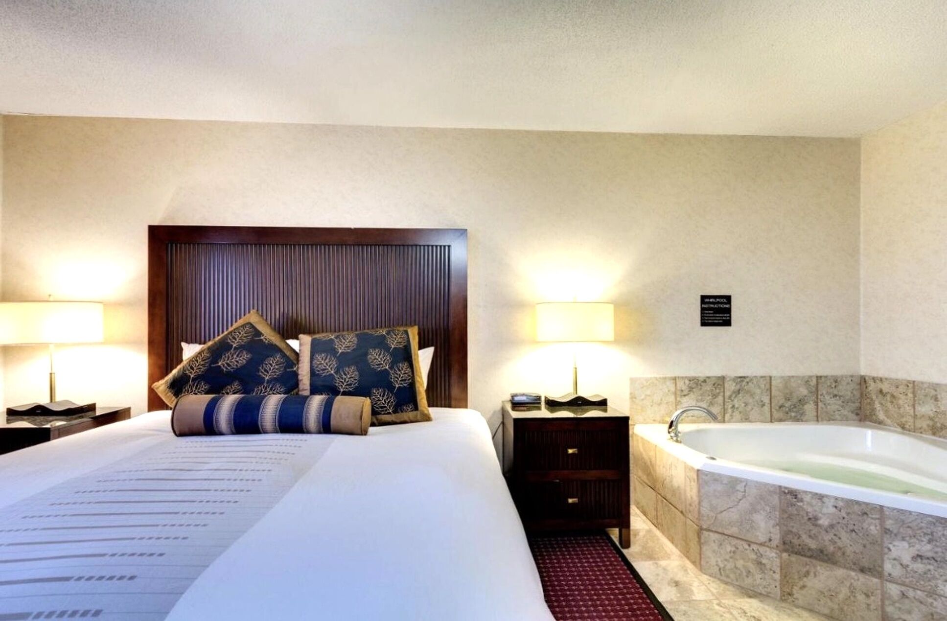 Habitación de hotel con una cama grande, dos mesitas de noche, un tocador, un televisor montado en la pared y una bañera.