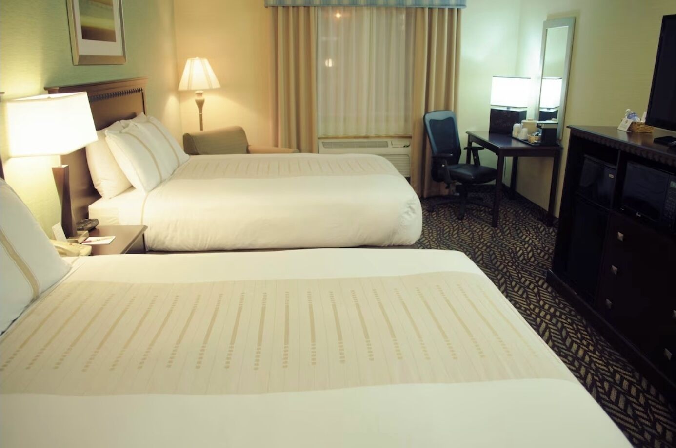 A hotel room with two beds, a desk with a chair, a TV, and a dresser.