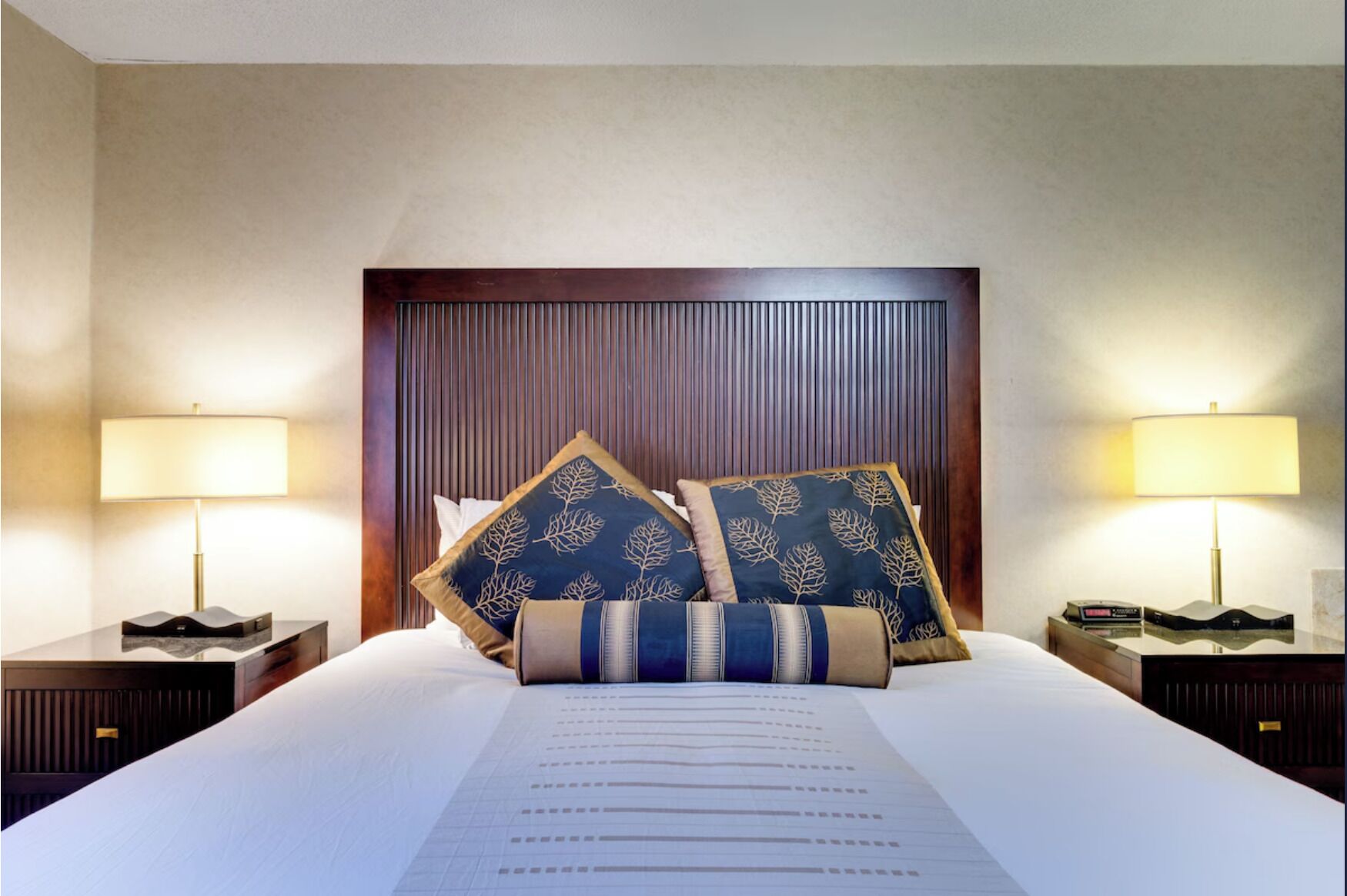 Une chambre d’hôtel avec un grand lit, deux tables de chevet, une tête de lit en bois et deux lampes.