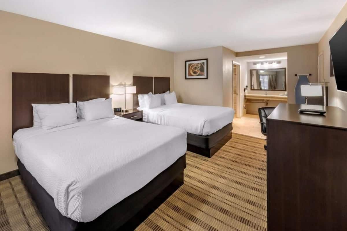 A hotel room with two beds, a desk, a mirror, and a television.
