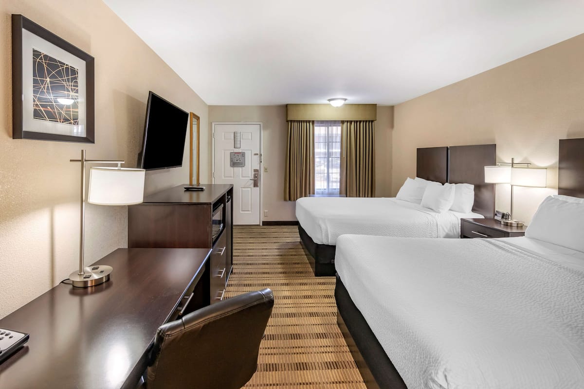 A hotel room with two beds, a desk, a chair, a TV, and a framed picture on the wall.