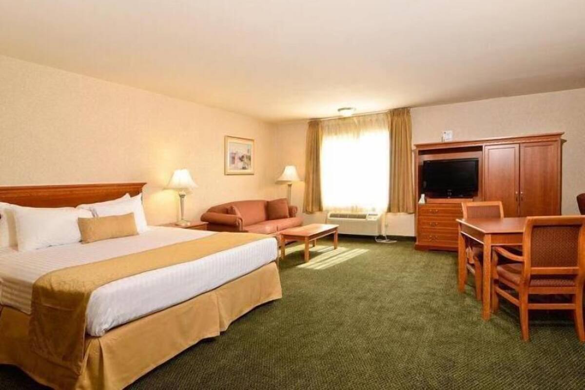 Een hotelkamer met een bed, een bank, een bureau, een televisie en een raam met gordijnen.