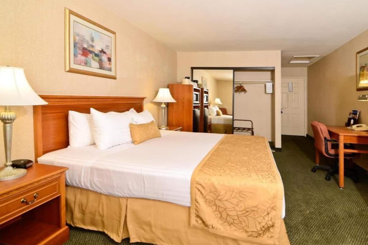 A hotel room with a bed, bedside table, lamp, desk, chair, and a mirror.
