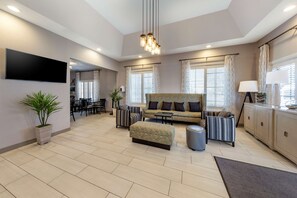 A modern living room with a sofa, ottoman, and a dining area in the background.