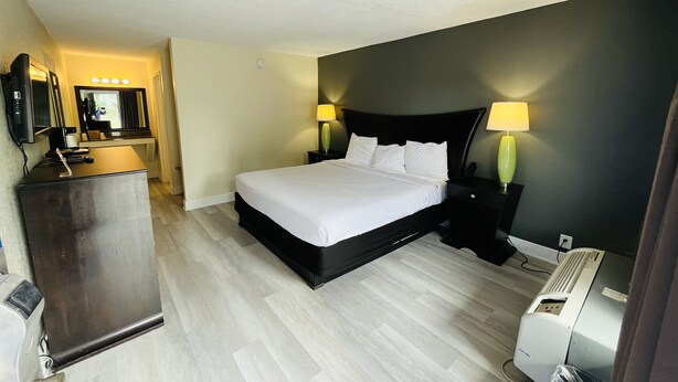 Una habitación de hotel con cama, lámparas de noche, escritorio con espejo y un calentador.