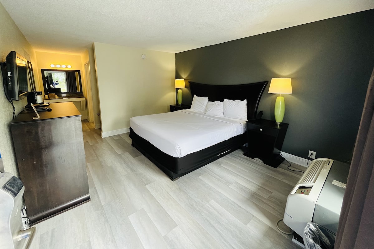 Una habitación de hotel con cama, lámparas de noche, escritorio con espejo y un calentador.