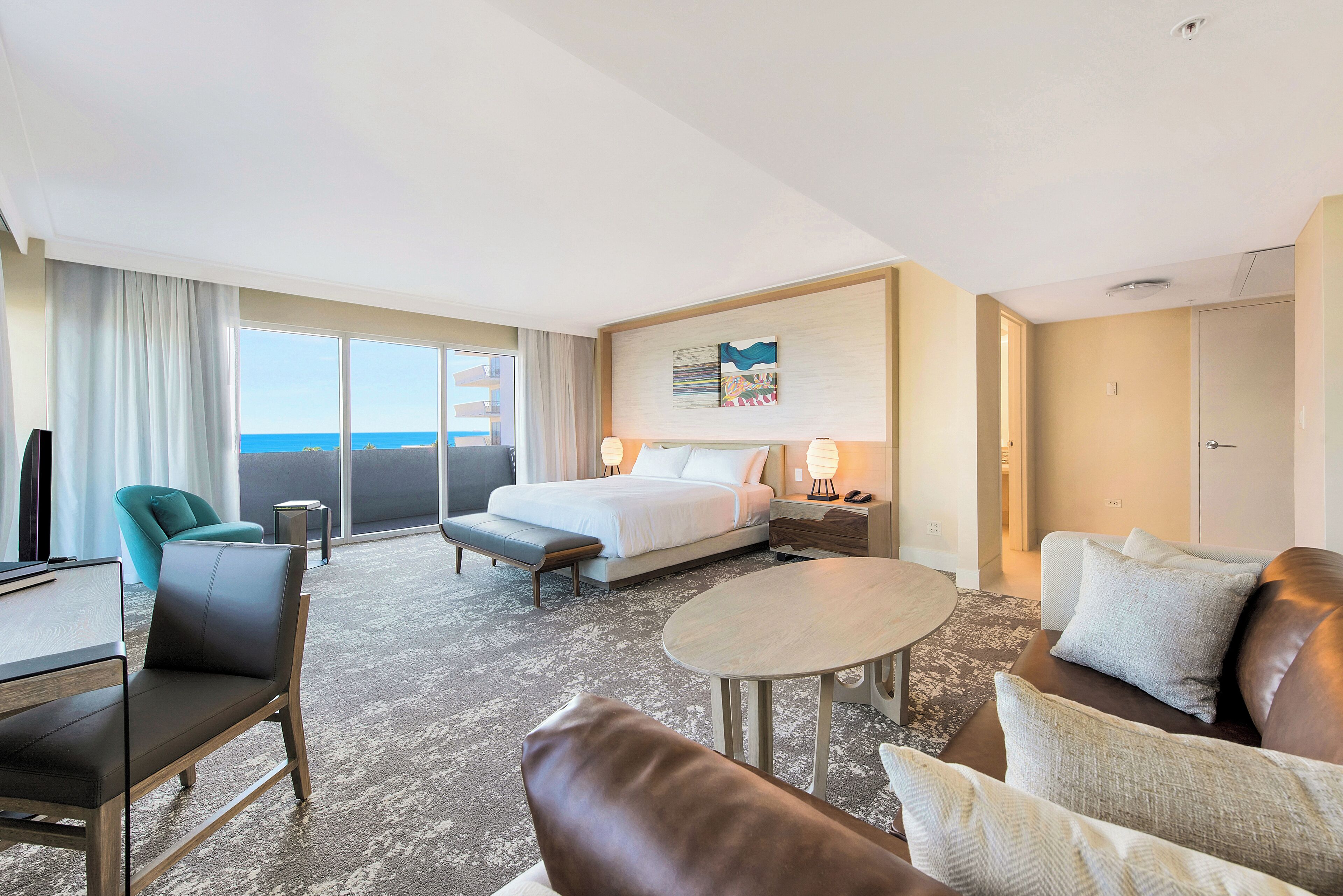 Ein Hotelzimmer mit Bett, Sofa, Schreibtisch, Stuhl, Tisch und einem Balkon mit Meerblick.