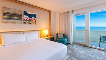Camera d'albergo con un letto grande, un comodino con una lampada, una sedia e una porta vetrata scorrevole che dà su un balcone con vista sull'oceano.