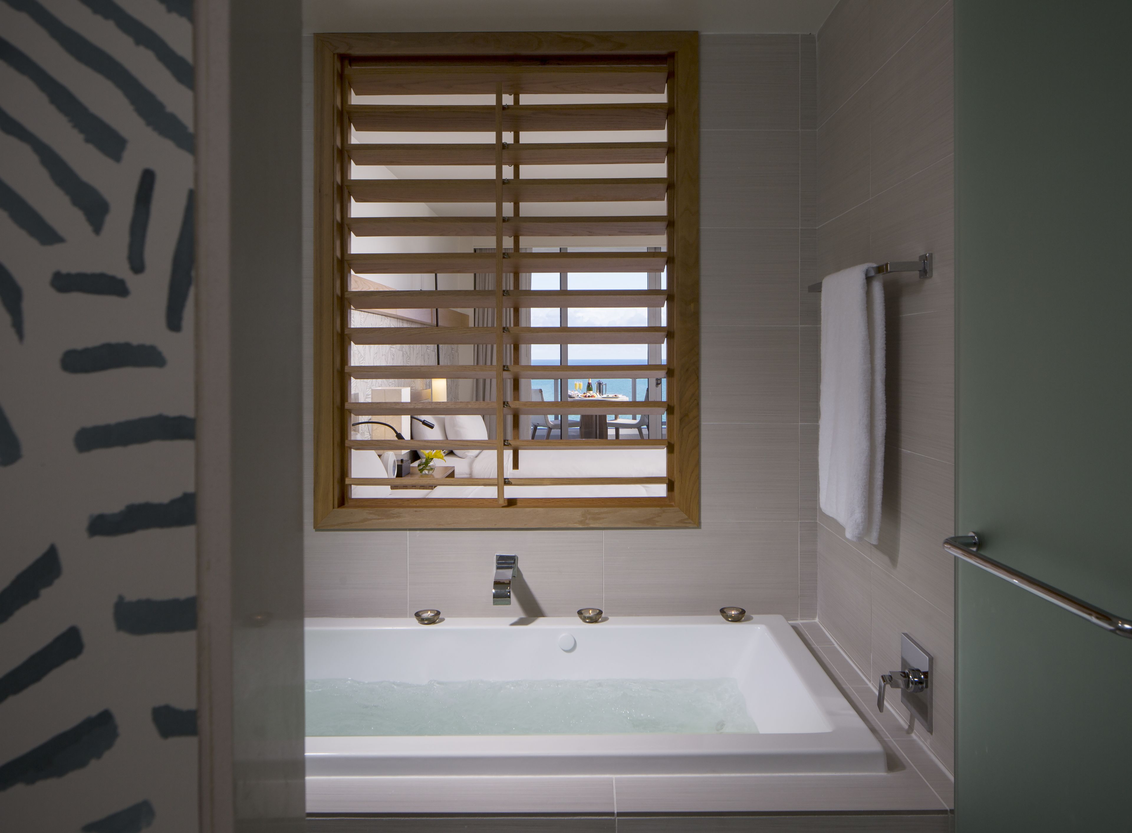 Une salle de bain moderne avec une baignoire sur pieds, une fenêtre avec des stores en bois et une vue sur la mer.