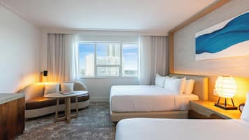 Ein Hotelzimmer mit zwei Betten, einem Sofa, einem kleinen Tisch, einer Lampe und einem großen Fenster mit Blick auf Gebäude.