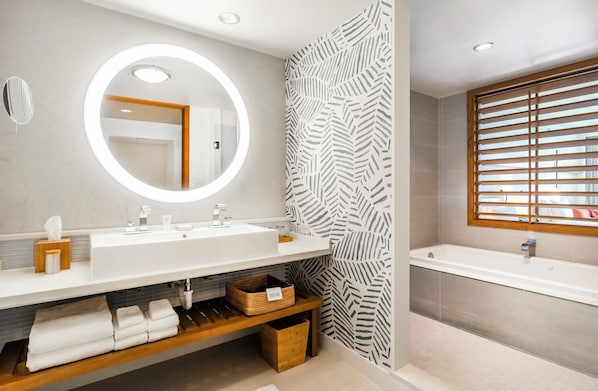 Une salle de bain moderne avec un grand miroir, deux lavabos, une baignoire et une étagère en bois où sont posées des serviettes.