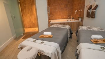 Um quarto de spa moderno, com duas camas, uma parede de madeira, uma banheira e toalhas.
