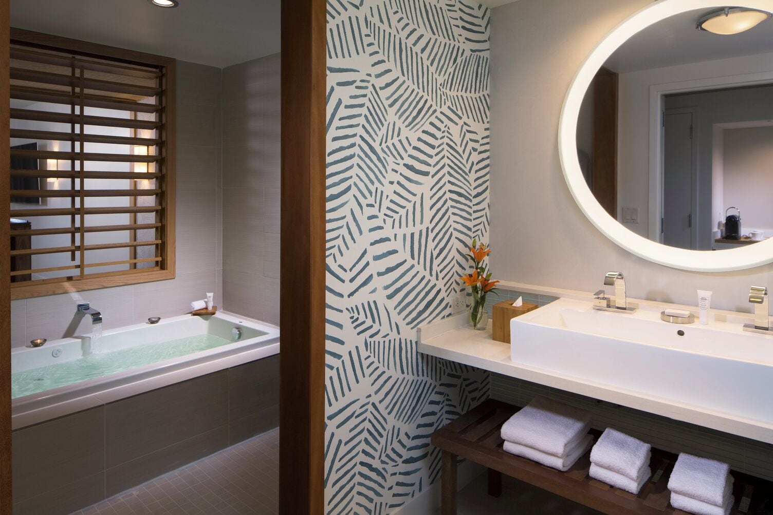 A bathroom with a bathtub, a sink with a mirror, and a wooden bench with towels.