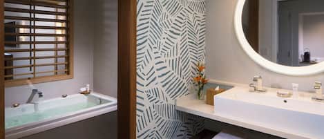 A bathroom with a bathtub, a sink with a mirror, and a wooden bench with towels.