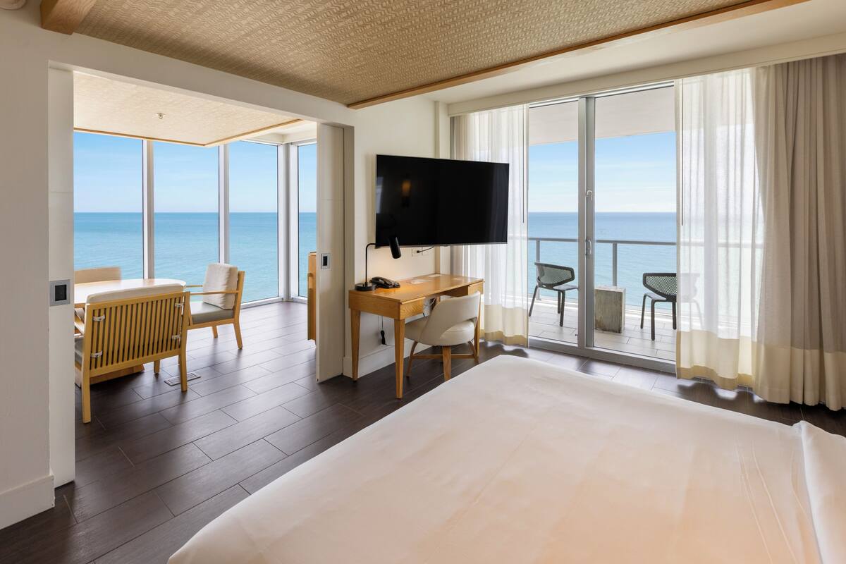 Habitación de hotel con una cama grande, un escritorio con silla, televisión y balcón con vista al mar.